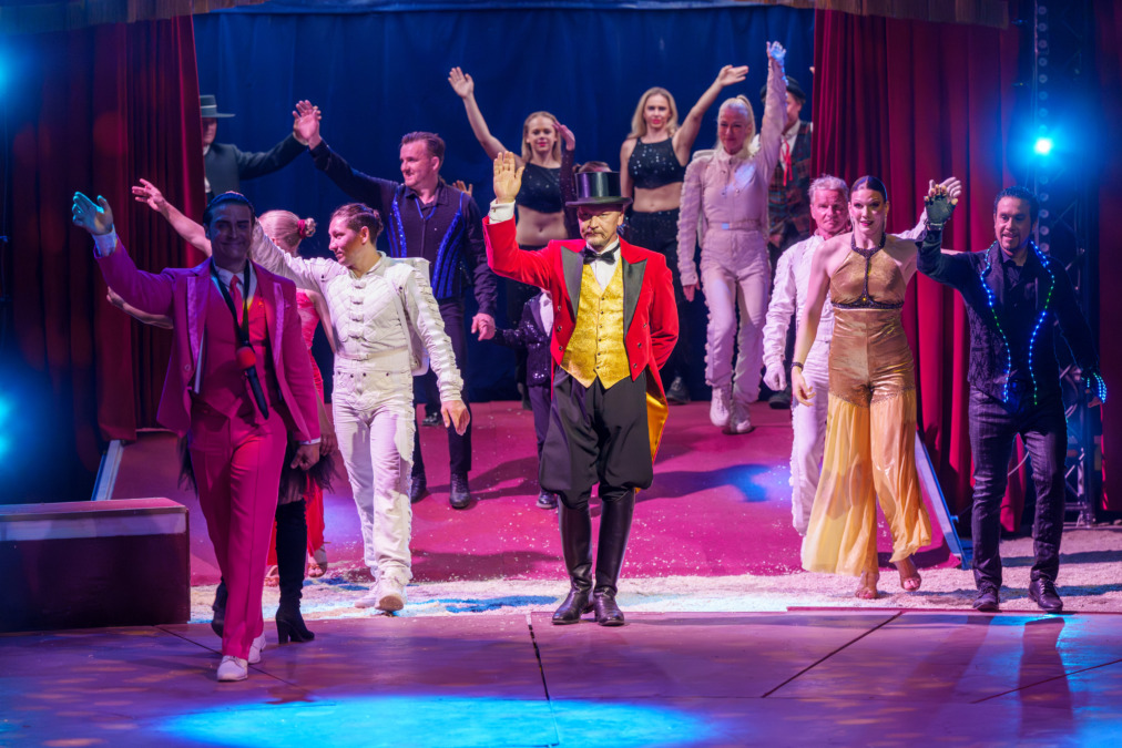 Sirkus Finlandian esiintyjät kumartavat ja vilkuttavat näytöksen päätteeksi maneesilla, etualalla juontaja frakissa ja silinterihatussa.